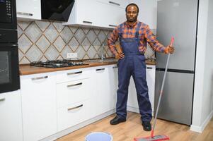 profissional limpador dentro azul uniforme lavando chão e limpando poeira a partir de a mobília dentro a vivo quarto do a apartamento. limpeza serviço conceito foto