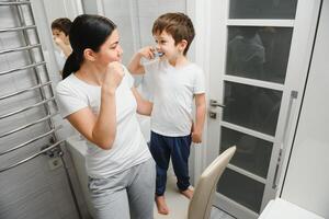 sorridente mãe e criança filho escovar dentes dentro banheiro foto