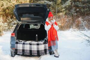 com copo do bebida. lindo jovem mulher é ao ar livre perto dela automóvel às inverno tempo. foto