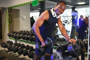 Preto masculino atleta levando haltere a partir de prateleira às Academia foto