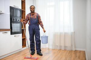 jovem africano homem lavagens a chão com uma esfregão dentro a quarto foto