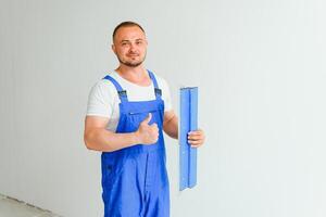 retrato do uma trabalhador dentro macacão e segurando uma massa de vidraceiro faca dentro dele mãos contra a gesso parede fundo. reparar trabalhos e construção conceito foto