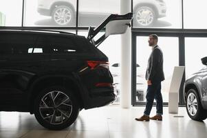 visitando carro concessionária. bonito barbudo homem é acariciando dele Novo carro e sorridente foto