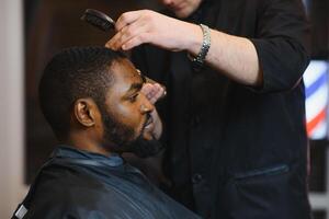 fechar-se do processo do aparar do cabelo dentro barbeiro fazer compras. qualificado barbeiro guardando tosquiadeira dentro mãos e corrigindo forma do cabelo para masculino cliente sentado em cadeira. conceito do corte de cabelo e barbear. foto