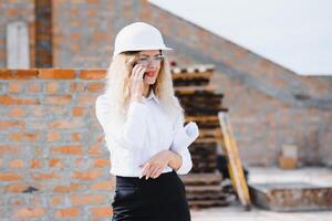 absorvido dentro a trabalhos do uma mulher engenheiro trabalhando com uma tábua em a fundo do a construção local. retrato do uma jovem arquiteto, protetora equipamento. seletivo foco foto