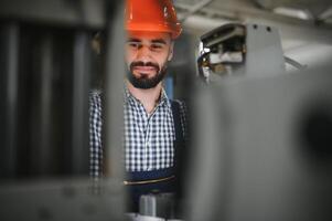 retrato do profissional pesado indústria engenheiro trabalhador vestindo segurança uniforme, Difícil chapéu sorridente. dentro a fundo desfocado ampla industrial fábrica. foto