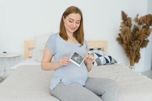 grávida mulher olhando às dela bebê sonografia. feliz expectante senhora desfrutando primeiro foto do dela por nascer criança, antecipando dela futuro vida, cópia de espaço