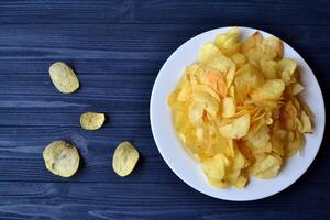 salgadinhos dentro a branco prato em a azul de madeira mesa. velozes Comida. frito batatas. foto