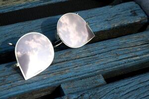 oculos de sol em uma azul de madeira backgorund. a céu é refletido dentro oculos escuros. foto