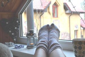 pernas dentro meias. mulher relaxante às casa perto a janela. decoração dentro a vivo sala. foto