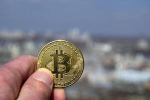 dourado bitcoin dentro masculino mão em borrado cidade fundo. homem segurando uma moeda do criptomoeda. foto