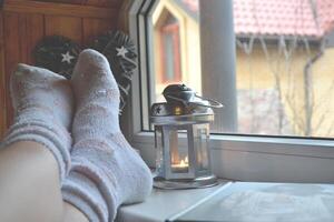 pernas dentro meias. mulher relaxante às casa perto a janela. decoração dentro a vivo sala. foto