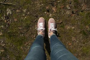 fêmea pernas dentro jeans e Rosa tênis em pé dentro uma terra do floresta. foto