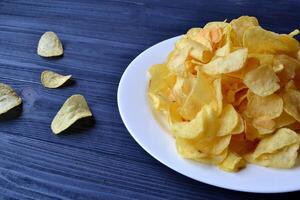 salgadinhos dentro a branco prato em a azul de madeira mesa. velozes Comida. frito batatas. foto