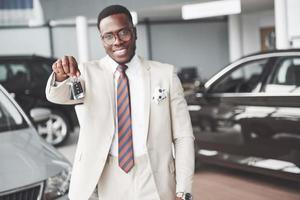 o jovem empresário negro e atraente compra um carro novo, ele tem as chaves na mão. sonhos se tornam realidade