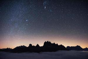 lindo espaço cheio de estrelas no céu. as montanhas estão rodeadas por nevoeiro denso foto