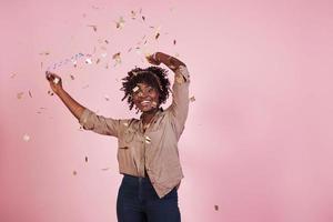 concepção do partido. jogando o confete para o ar. mulher afro-americana com fundo rosa atrás