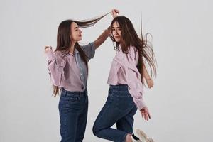 brincando com o cabelo. duas irmãs gêmeas em pé e posando no estúdio com fundo branco foto