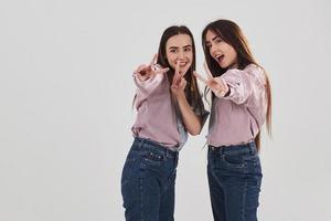 garotas alegres se divirtam. duas irmãs gêmeas em pé e posando no estúdio com fundo branco foto