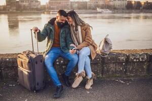 feliz casal turistas estão usando Móvel telefone enquanto sentado e em repouso em seus período de férias com seus bagagem. foto