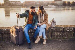 feliz casal turistas estão usando Móvel telefone enquanto sentado e em repouso em seus período de férias com seus bagagem. foto