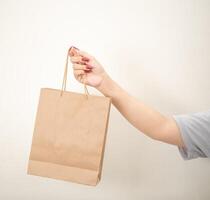mão segurando uma compras papel saco contra uma branco isolado fundo foto