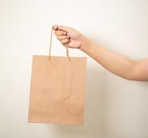 mão segurando uma compras papel saco contra uma branco isolado fundo foto
