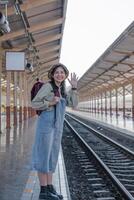 jovem ásia mulher dentro moderno trem estação fêmea mochileiro passageiro esperando para trem às trem estação para ir em feriado. foto