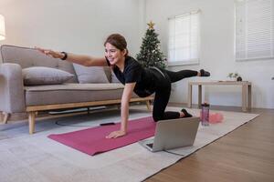 jovem ásia desportivo ginástica mulher treinador Faz prática vídeo conectados Treinamento ioga computador portátil dentro vivo quarto às casa foto