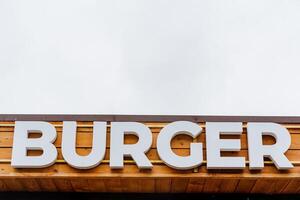 hamburguer restaurante logotipo, hamburguer palavra placa dentro branco cartas, texto escrito em uma árvore fundo, rua restaurante, carne comida, rua Comida foto