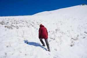 uma homem dentro uma vermelho Jaqueta sobe morro acima em pé. a alpinista sobe para a topo do a montanha dentro a neve. foto