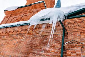 afiado pingentes de gelo em a cobertura do a construção.perigosa.remoção do pingentes de gelo a partir de a fachada. congeladas água. inverno natural fenômenos foto