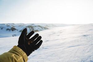 mão Preto luva contra a fundo do branco neve dentro inverno, uma homem esticado dele mão frente para Conheça a sol, a estendido Palma, uma turista em uma caminhar dentro a montanhas. foto