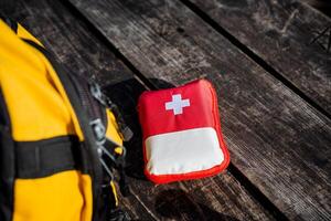 a primeiro ajuda kit é em a mesa, uma vermelho saco em uma de madeira fundo, fechar-se do medicação, emergência primeiro ajuda, uma pequeno primeiro ajuda kit. foto