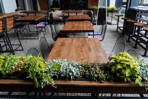 cafés em a rua, verde plantas decorar a restaurante, rua comida, de madeira mesa, não pessoas, esvaziar cadeiras, a ar livre cidade velozes Comida restaurante. foto