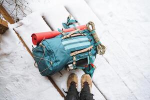 uma brilhante caminhada mochila mentiras em a neve. uma escalada corda é amarrado para uma mochila. dentro a lado bolso do a garrafa térmica. caminhada dentro inverno. pedras e florestas foto