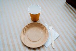 ecológico utensílios de cozinha para comida, uma prato do papel em uma construir fundo, uma garfo fez do bambu. uma vidro para quente bebidas. eco produtos. conjunto do pratos. foto