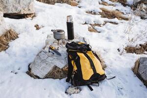 caminhada equipamento caminhada dentro inverno montanhoso terreno amarelo mochila garrafa térmica quente café Panela carrinhos em queimador gás faca sobrevivente equipamento turista foto