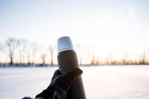 garrafa térmica dentro mão contra a céu. lindo conceptual foto do uma vácuo garrafa térmica. quente chá para beber dentro natureza.