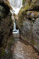 a corrente fluxos dentro uma limitar desfiladeiro entre a pedras. Kungurtui cascata dentro bashkortostan Rússia sulista Urais, Primavera inundar dentro a montanhas, passagem entre a rochas, foto