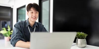 homem de negocios usando computador portátil computador dentro escritório, feliz jovem ásia homem de negocios dentro moderno escritório olhando em computador portátil foto