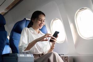 viajando e tecnologia. vôo às primeiro aula. jovem o negócio mulher passageiro usando Smartphone enquanto sentado dentro avião voar foto