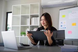 empreendedor ou o negócio mulher trabalhando comparando documentos com uma computador computador portátil sentado dentro uma escrivaninha às escritório foto