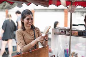 feliz jovem ásia viajante viciado em comida mulher ordem crepes às ao ar livre noite mercado rua Comida fornecedor foto