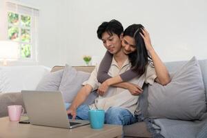 feliz casal ásia sentar relaxar em sofá dentro vivo quarto assistindo vídeo em computador portátil juntos às casa foto