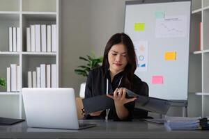 empreendedor ou o negócio mulher trabalhando comparando documentos com uma computador computador portátil sentado dentro uma escrivaninha às escritório foto