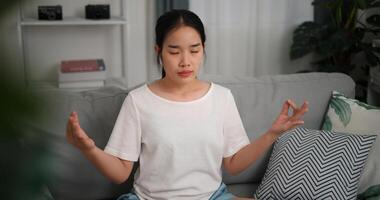 Alto ângulo visualizar, feliz jovem mulher vestem sem fio fones de ouvido meditando fazendo uma lótus pose às casa com olhos fechado, relaxante corpo e mente sozinho em sofá dentro a vivo quarto, relaxamento estilo de vida foto