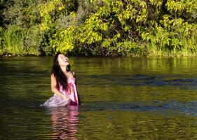 sorridente japonês americano mulher em pé dentro rio foto