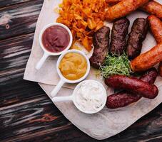 Cerveja conjunto do grelhado salsichas com cozido repolho e molhos foto