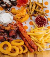 francês fritas batatas com cebola argolas, salsichas, croutons e picante frango pernas foto